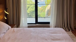 Et soveværelse med en stor seng, udsigt til vand og en balkon med gardiner.