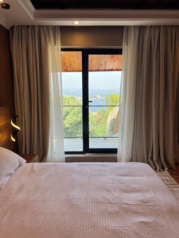 A bedroom with a large bed, a view of a body of water, and a balcony with curtains.