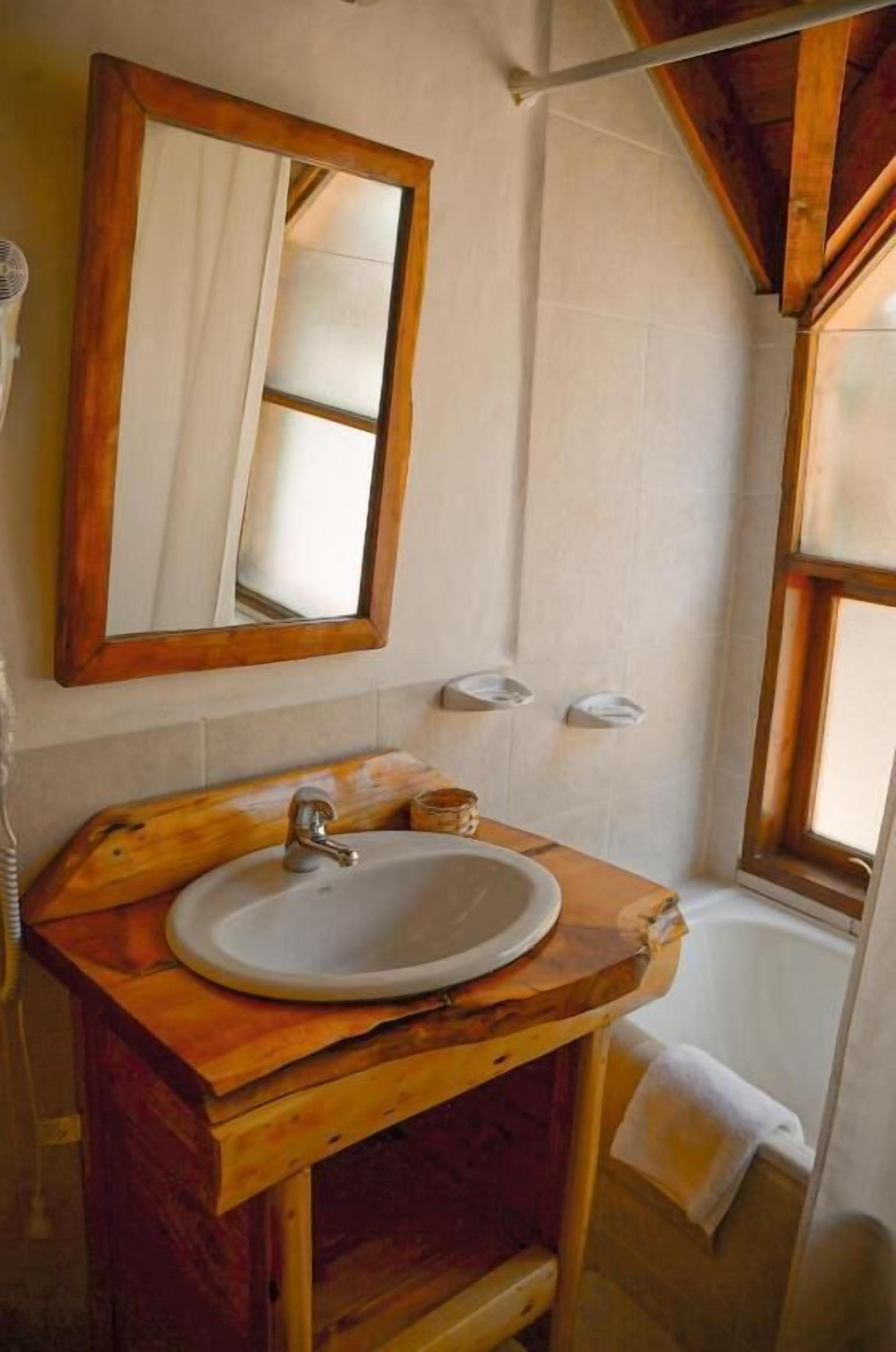 Un baño con tocador de madera, espejo, lavamanos, bañera y ventana.