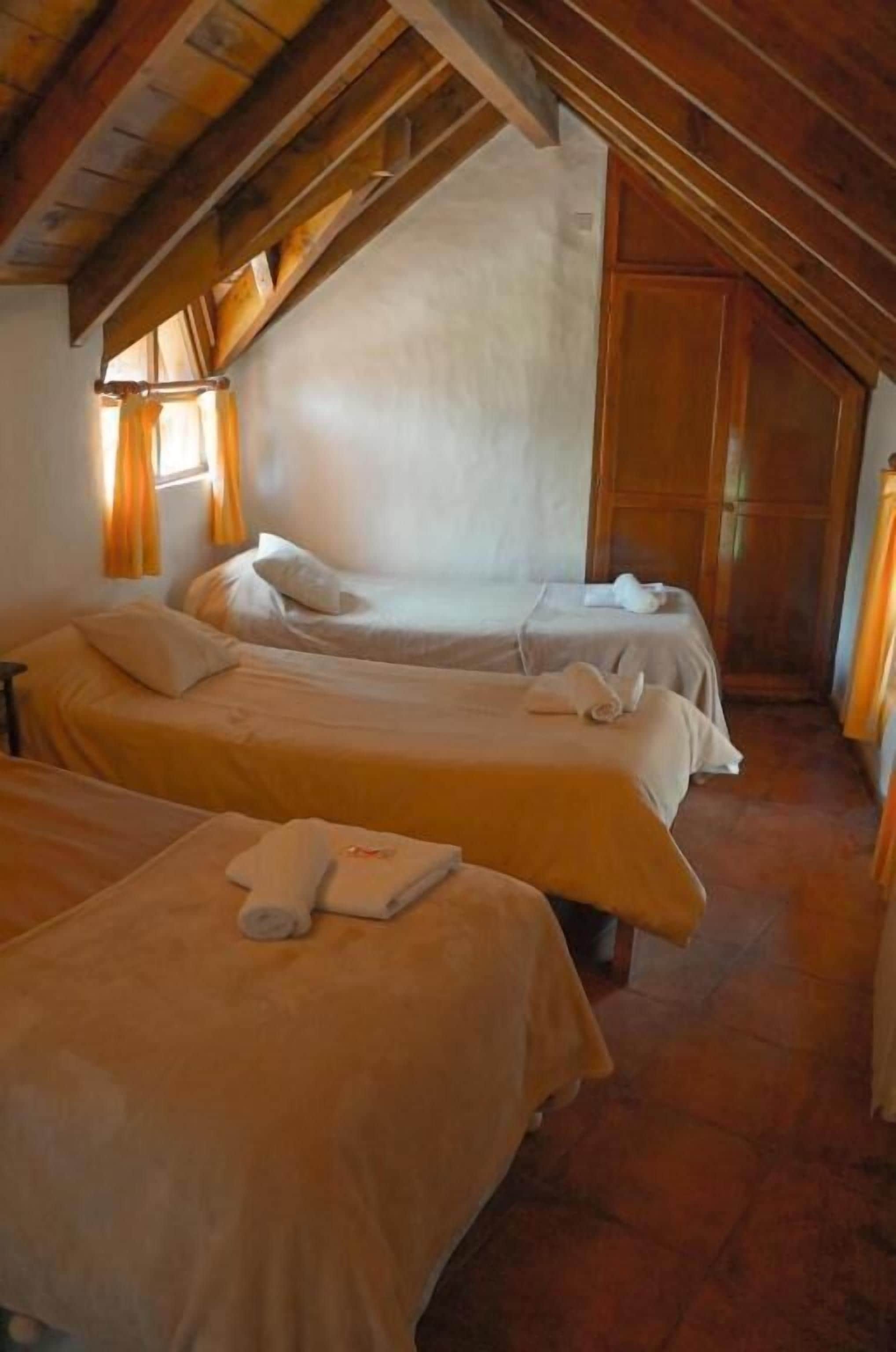 Una habitación con dos camas, vigas de madera en el techo, una ventana con cortinas y una puerta.