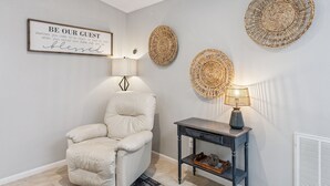 A room with a framed sign, a chair, a table with a lamp, and woven wall decorations. - Quiet, Clean and Beautiful 3/2 Retreat Near Everything! (Sanford)