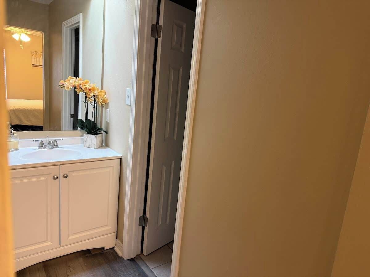 Un baño con tocador blanco, lavamanos, espejo y una puerta que da a otra habitación.