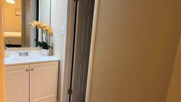 Un baño con tocador blanco, lavamanos, espejo y una puerta que da a otra habitación.