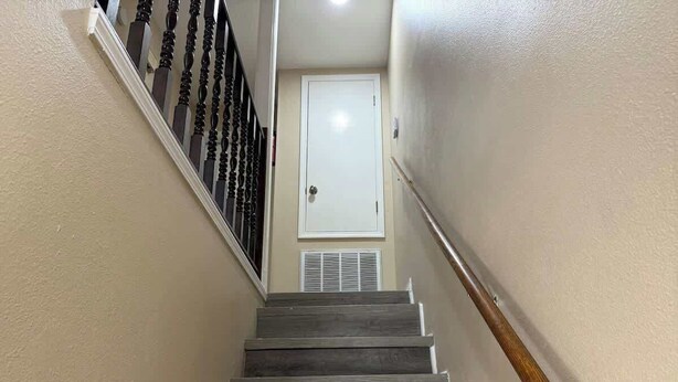 Una escalera de madera con barandilla, una puerta blanca en la parte superior y una rejilla en la pared.