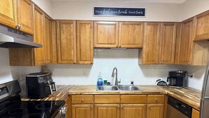 Una cocina con armarios de madera, un lavamanos de acero inoxidable, una cafetera y un lavavajillas.