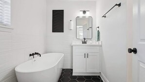 Un baño con una bañera independiente, un tocador blanco con espejo y un piso de baldosas blanco y negro.