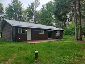 A small, single-story cabin with a front door, a covered patio, and a garage.