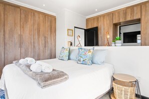 Un dormitorio con una cama grande, un armario de madera, lámparas de noche y una mesita redonda.
