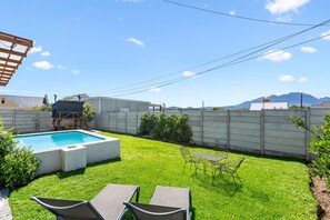 Un patio trasero con piscina, zona de barbacoa techada y un área de estar con sillas y una mesa.