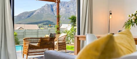 A room with a view of mountains, a pool, and outdoor furniture.