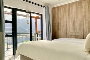 A bedroom with a bed, a wooden wardrobe, and a balcony with a view of mountains.