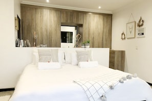 A bedroom with a large bed, wooden wardrobe, and a small window.