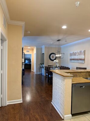 A kitchen with a central island, a dining area with a chandelier, and a hallway leading to another room. - 3BR Disney Oasis /Sleeps 8 /No Fees (Davenport)
