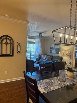 A dining area with a glass table, chairs, a chandelier, and a view into the living room. - 3BR Disney Oasis /Sleeps 8 /No Fees (Davenport)