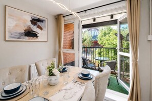 A dining area with a table set for four, a view of the garden through a glass door, and a painting on the wall. - Cosy City Centre | Modern | 3Bed | Balcony (Manchester)