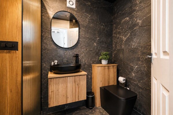 A bathroom with a black sink, wooden vanity, a mirror, a potted plant, and a toilet. - Cosy City Centre | Modern | 3Bed | Balcony (Manchester)
