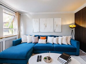 A modern living room with a blue sectional sofa, a round coffee table, and a floor lamp. - 3 Bedroom |City Centre | Modern  with Balcony (Manchester)