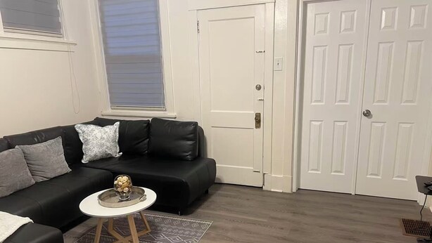 A living room with a black leather sofa, a small round table with a decorative bowl, a patterned rug, and a white door. - Modern 2BR • 2 King Beds • Near Bakery Sq, Downtown & Universities (Pittsburgh)