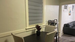 A dining area with a table and chairs, a window with blinds, a black leather couch, and a small plant on the table. - Modern 2BR • 2 King Beds • Near Bakery Sq, Downtown & Universities (Pittsburgh)