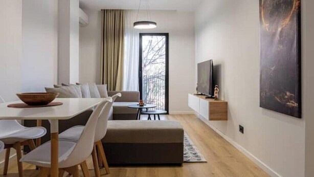 A modern living room with a dining area, a sofa, a TV, and artwork on the wall. - Barrikada-E – Central Apartments with French Balcony in Tirana (Tiranë)