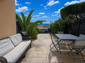 Eine Terrasse mit einer Couch, Tisch, Stühlen, einem Grill und Blick auf das Meer.