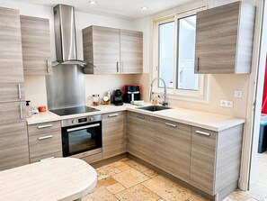 A modern kitchen with a built-in oven, a stainless steel range hood, a coffee maker, and a window above the sink. - REF ESTEREL BY PALMES D OR PROPERTIES (Mandelieu-la-Napoule)