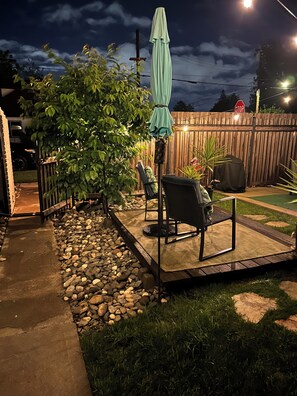 Ein Hinterhof mit einer Terrasse, einem Tisch, Stühlen, einem schattenspendenden Sonnenschirm, einem Holzzaun und einem Stoppschild im Hintergrund.