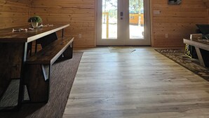 A spacious loft with a high ceiling, wooden walls, a large dining table, and a door leading outside.