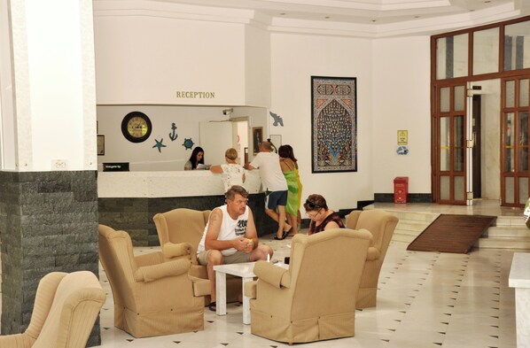 A reception area with a reception desk, seating area with chairs and tables, decorative wall art, and a patterned floor. - Green Peace Hotel Alanya  (Alanya)