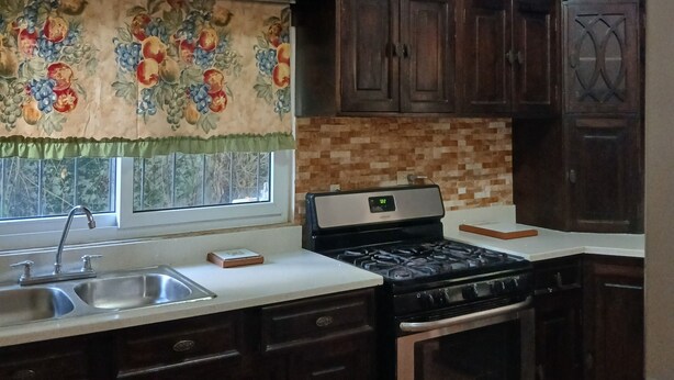 Une cuisine avec des meubles de rangement en bois foncé, un évier en acier inoxydable, une cuisinière et un réfrigérateur.