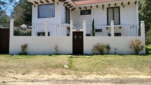 Une maison à deux étages, avec une façade blanche, un toit recouvert de tuiles et un portail noir.