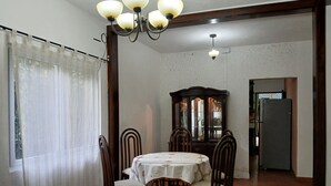 Un coin repas comprenant une table ronde, des chaises, un lustre, un buffet aux portes vitrées et une fenêtre avec des rideaux.