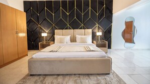 A modern bedroom with a large bed, wooden wardrobe, and a unique wall design. - THE CARRINGTON SUITES (Lagos)