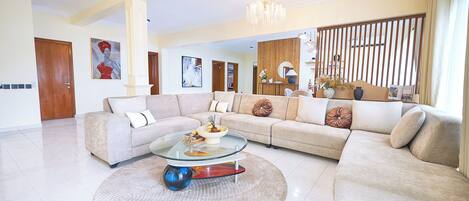A spacious living room with a large sectional sofa, a glass coffee table, and a chandelier.
