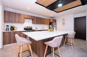 A modern kitchen with wooden cabinets, a white countertop, and two bar stools. - Summer House Azul - Private swimming pool - 3 rooms (Jacó)