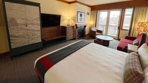 Ein Hotelzimmer mit einem großen Bett, einem Schreibtisch, einem Stuhl, einem kleinen Tisch, einem Kamin und einem Balkon mit Vorhängen.
