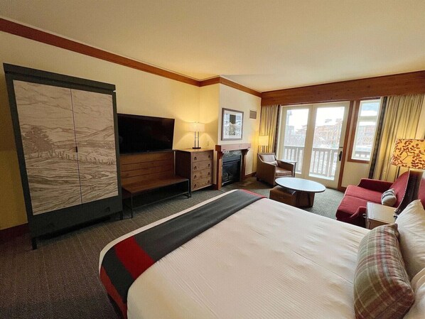 A hotel room with a large bed, a desk, a chair, a small table, a fireplace, and a balcony with curtains. - Cozy Ski-In/Ski-Out Stowe Lodge studio with Hot Tub, Views, & Fireplace (Stowe)