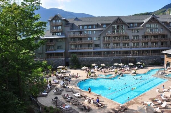 Un hotel de varios pisos, con piscina y montañas al fondo.