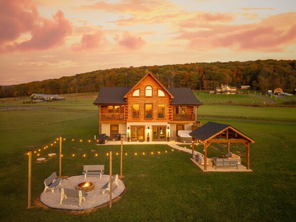 A two-story log cabin with a deck, outdoor seating, and a fire pit. - Brand New Cabin w Hot Tub, Fishing Pond, Firepit (McHenry)