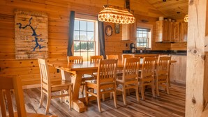 A wooden cabin interior with a dining table, chairs, a kitchen area, and a map on the wall. - Brand New Cabin w Hot Tub, Fishing Pond, Firepit (McHenry)