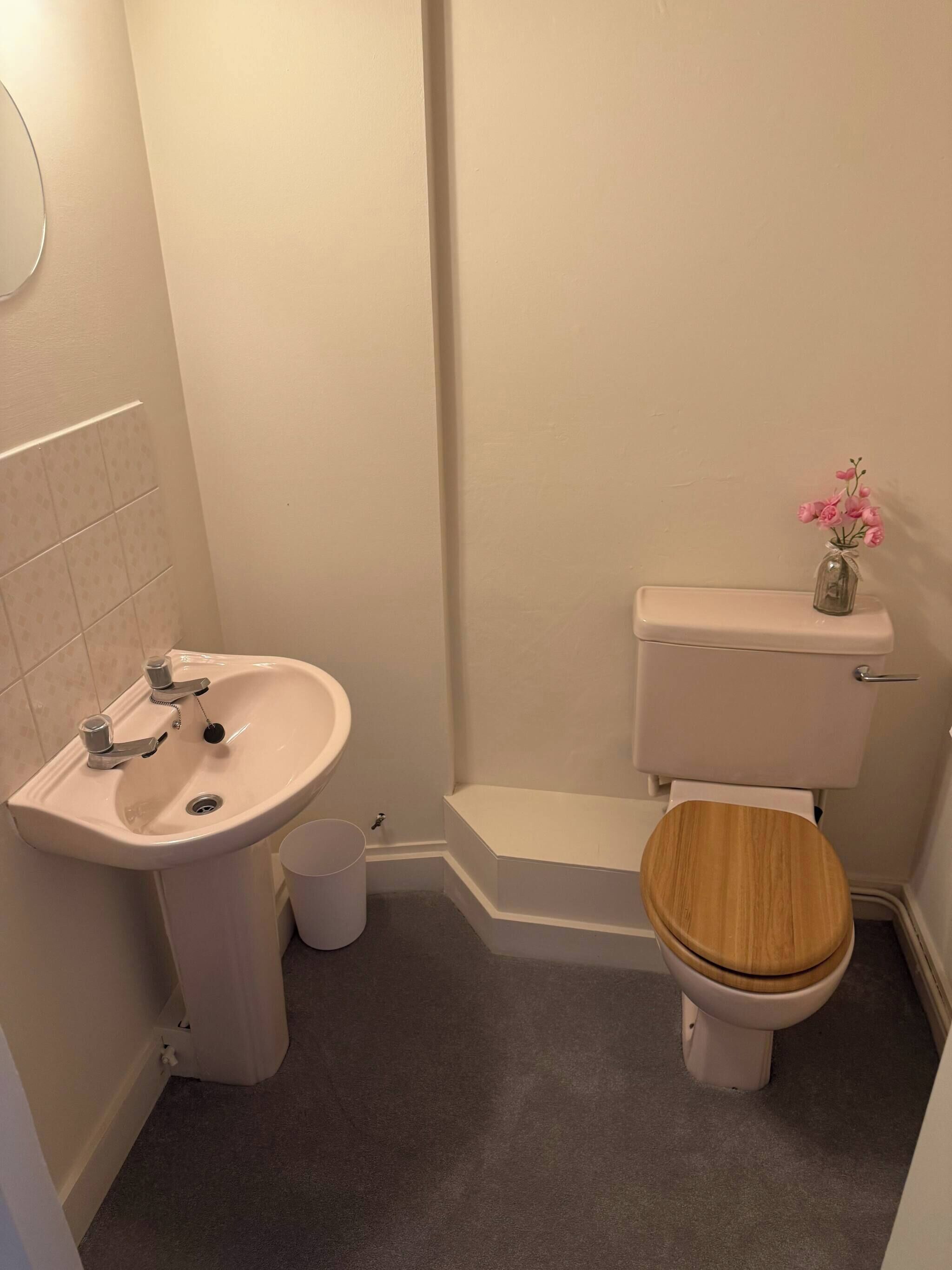 Un baño con lavamanos, inodoro y un pequeño florero con flores sobre el tanque del inodoro.