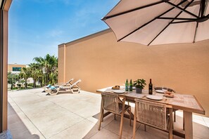 A patio with a table set for dining, lounge chairs, and a large umbrella.