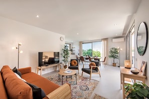 A modern living room with a sofa, TV, dining area, and large windows.