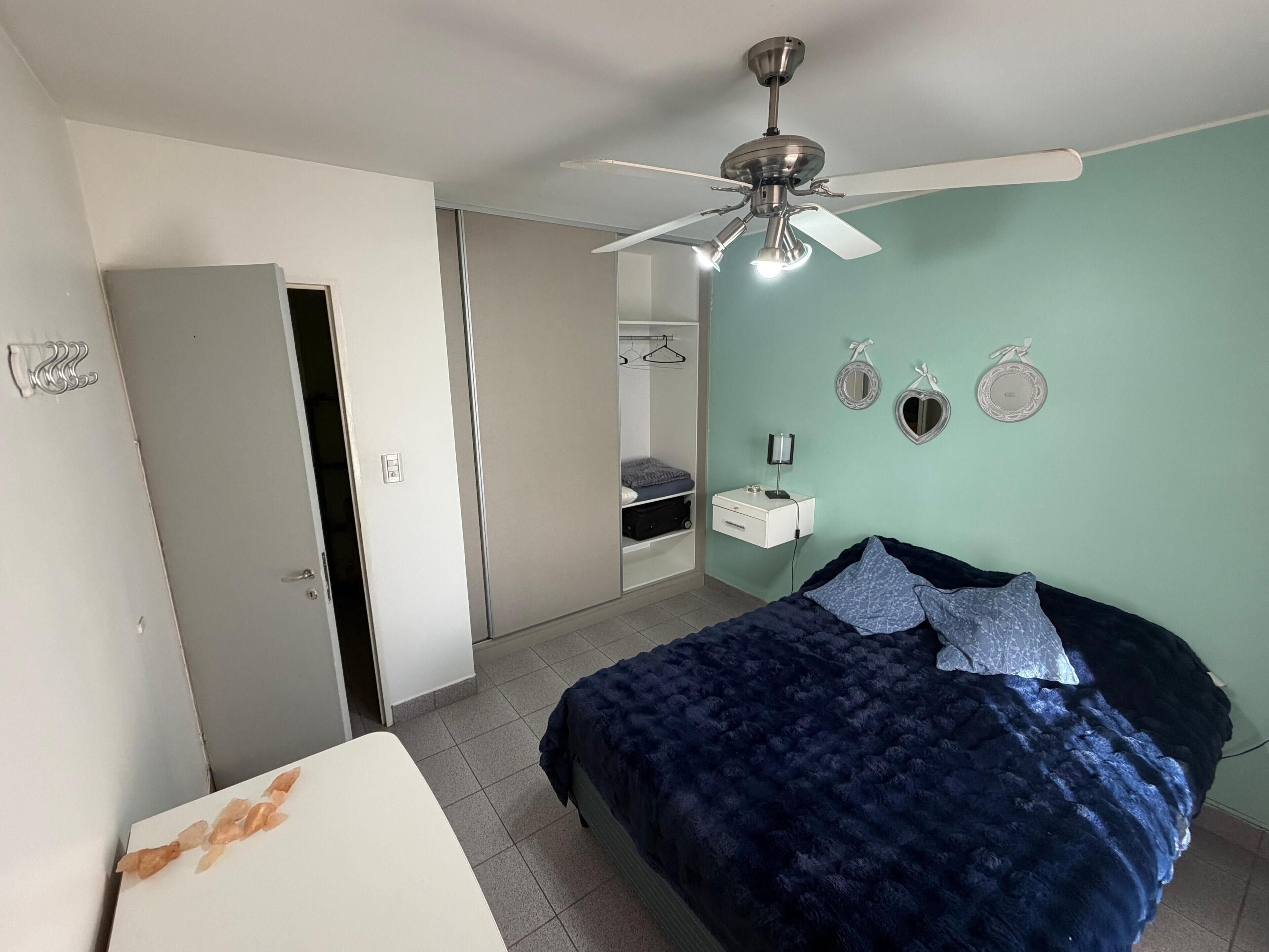 Une chambre à coucher comprenant un lit, une armoire, un ventilateur de plafond et une table de chevet.