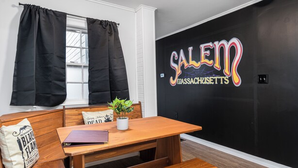 A room with a wooden table, bench, black curtains, a potted plant, and a wall with 'Salem Massachusetts' signage.