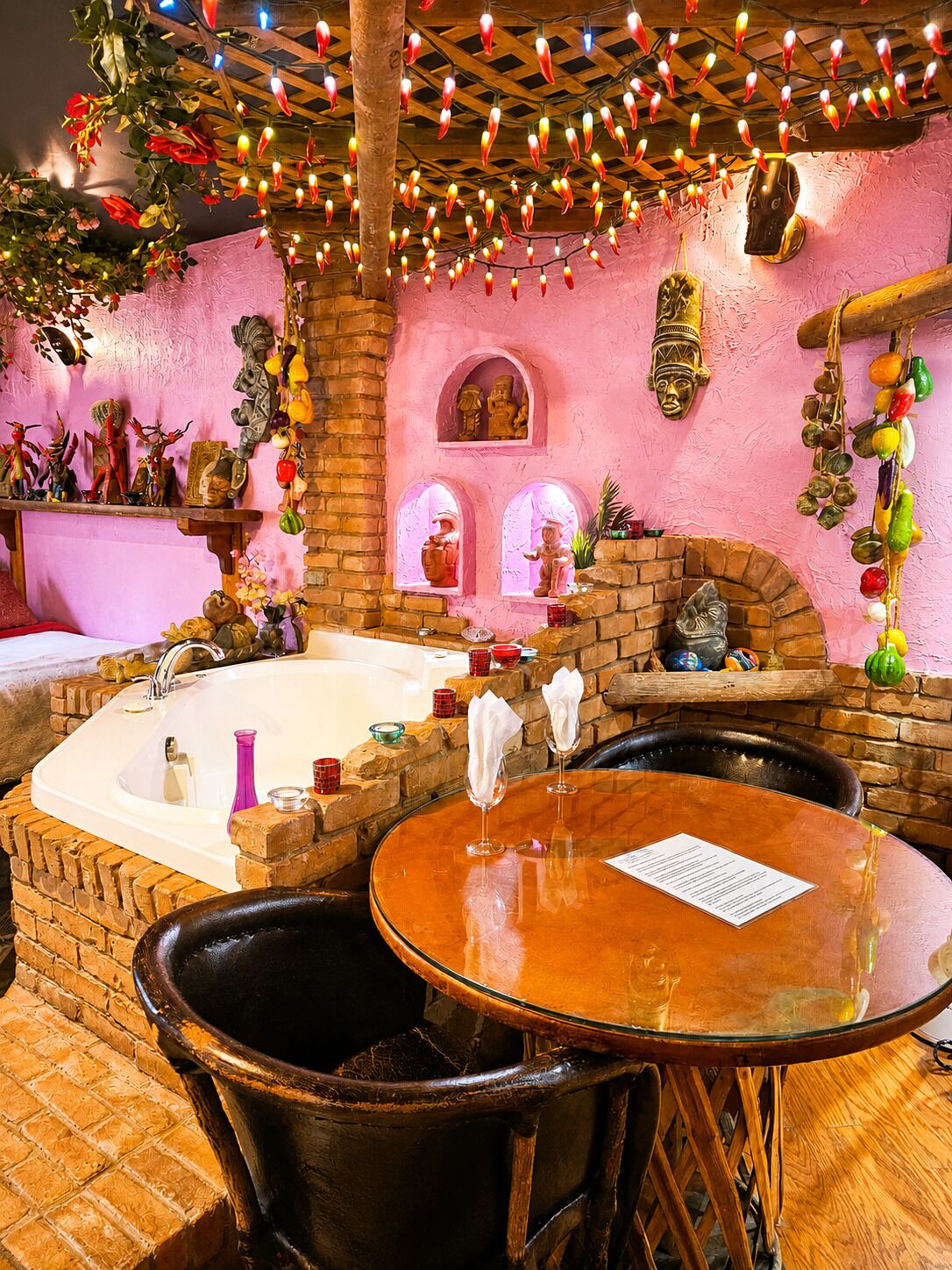 A room with a brick wall, a bathtub, a wooden table, and a chair.