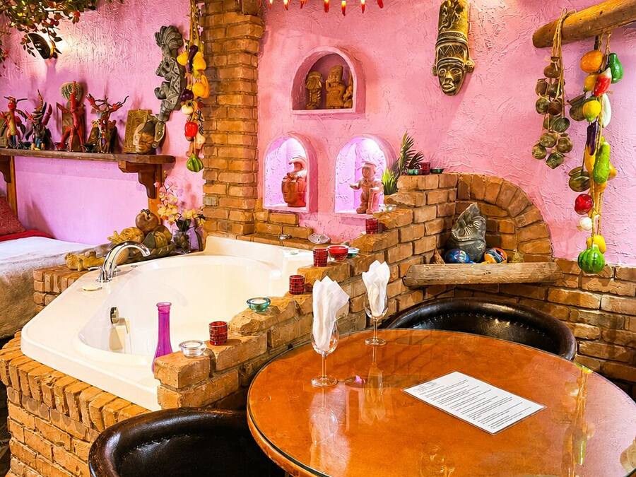 A room with a brick wall, a bathtub, a wooden table, and a chair.