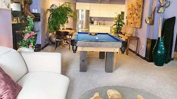 En opholdsstue med billardbord, sofa, sofabord i glas med en skildpaddeskulptur og et farverigt loftsmaleri.