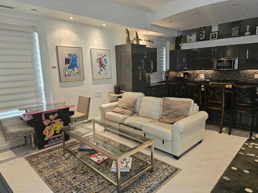 A modern living room with a glass coffee table, a white sofa, and a kitchen area with dark cabinetry and a microwave.