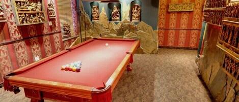 A pool table with balls, surrounded by patterned wallpaper and decorative items.
